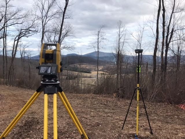 Surveying equipment set up on a wooded hillside overlooking a mountain valley